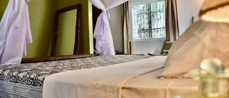 Una cama con una colcha estampada, una mesita de noche con una botella y una ventana con cortinas.