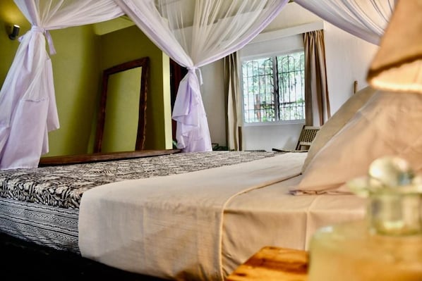 A bed with a patterned bedspread, a bedside table with a bottle, and a window with curtains.