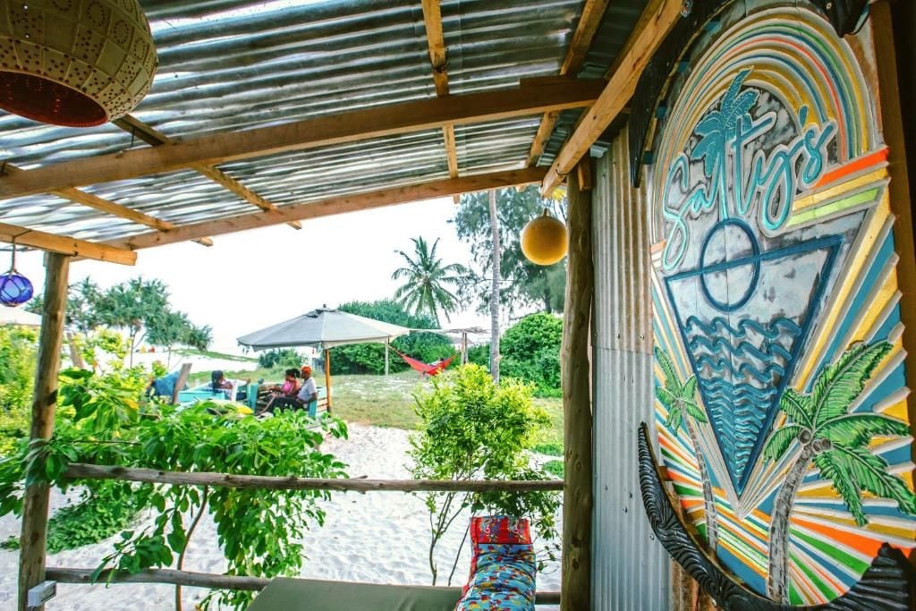 A beachside restaurant with a colorful mural, outdoor seating, and a view of the beach.
