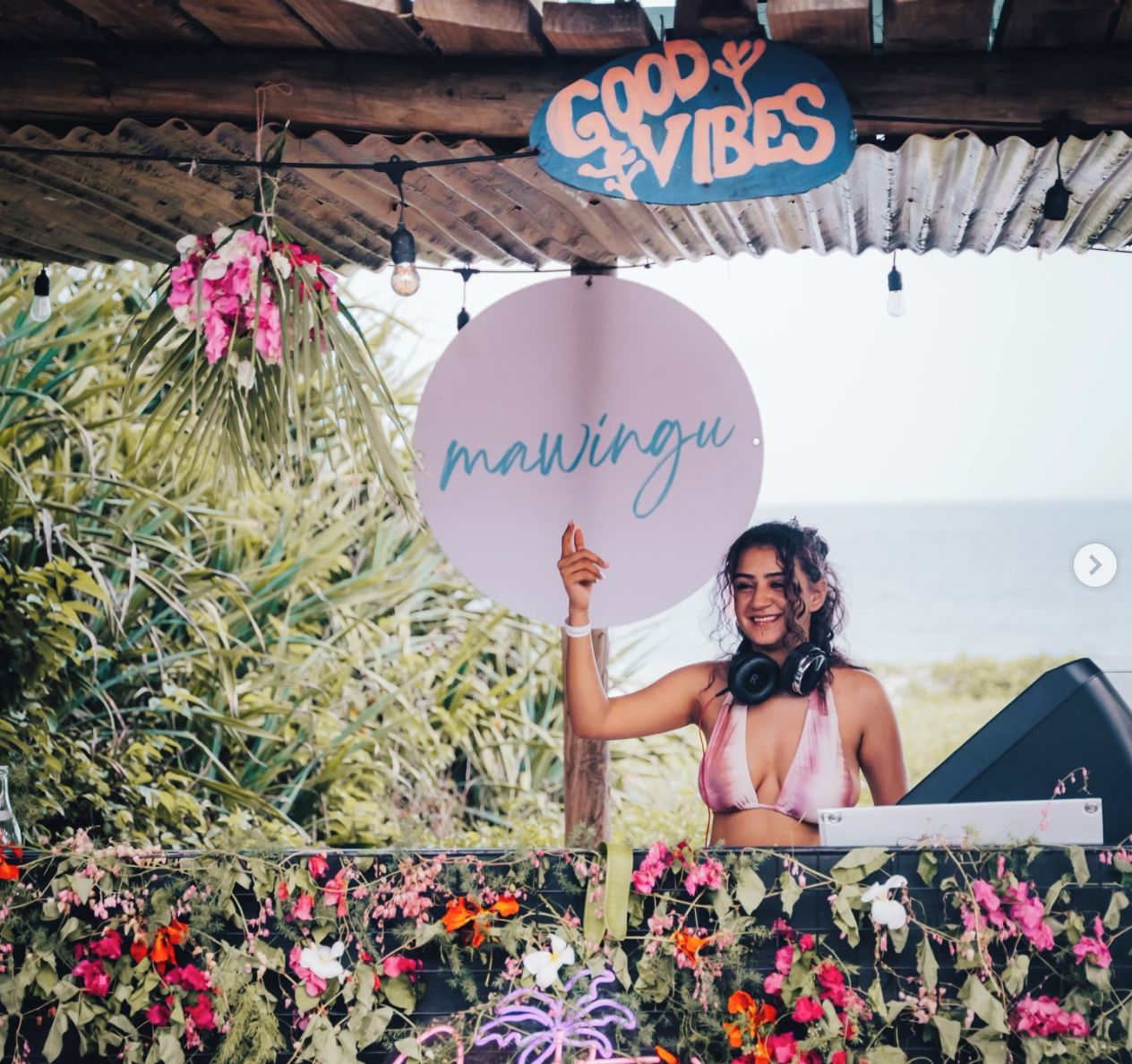 A person holding a sign with 'mawingu' written on it, standing under a wooden structure with a 'GOOD VIBES' sign.
