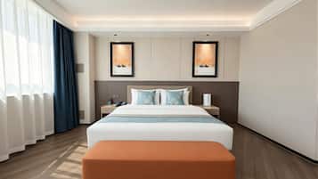 A hotel room with a large bed, a bedside table, a nightstand, a lamp, and a window with curtains.