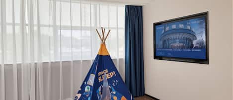 A room with a large window, a blue space-themed tent, and a framed picture on the wall.