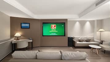 A modern hotel room with a sofa, a small table, a desk, a chair, a TV screen, and a lamp.
