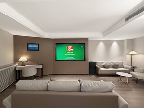 Una habitación de hotel moderna con sofá, una mesita, un escritorio, una silla, una pantalla de televisión y una lámpara.