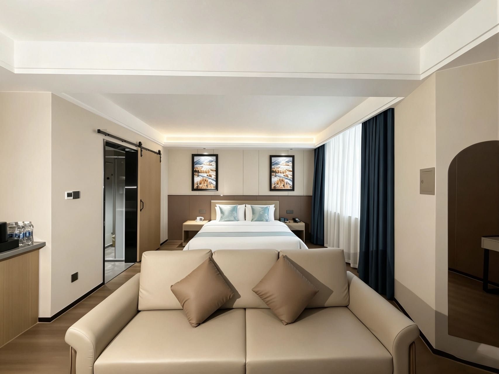A modern hotel room with a large bed, a sofa, a desk, and a minibar.