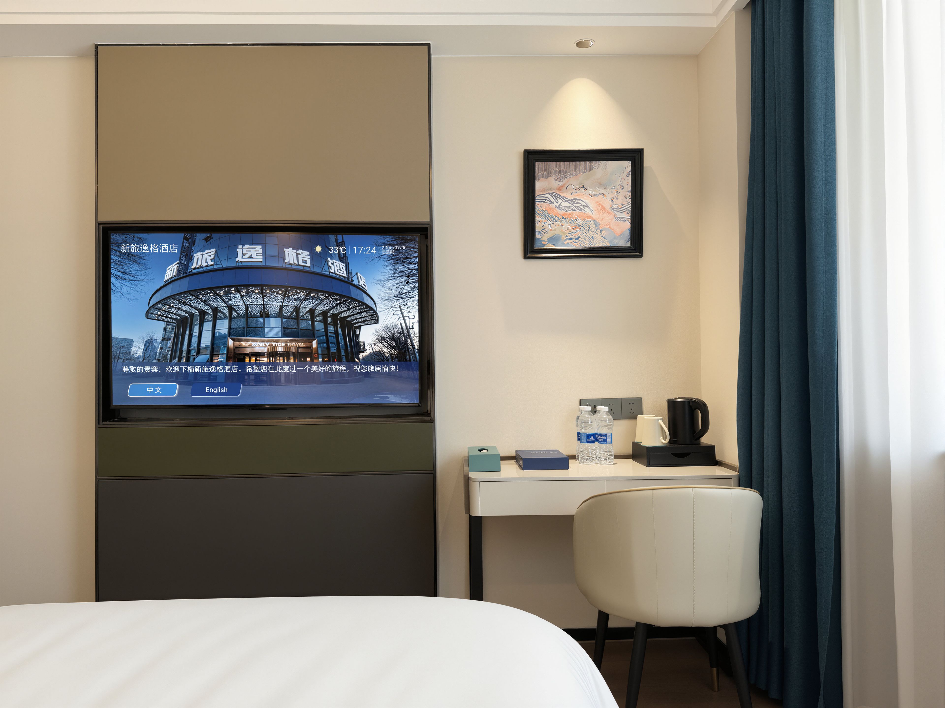 A hotel room with a bed, a desk with a chair, a television mounted on the wall, a framed picture, and a window with curtains.