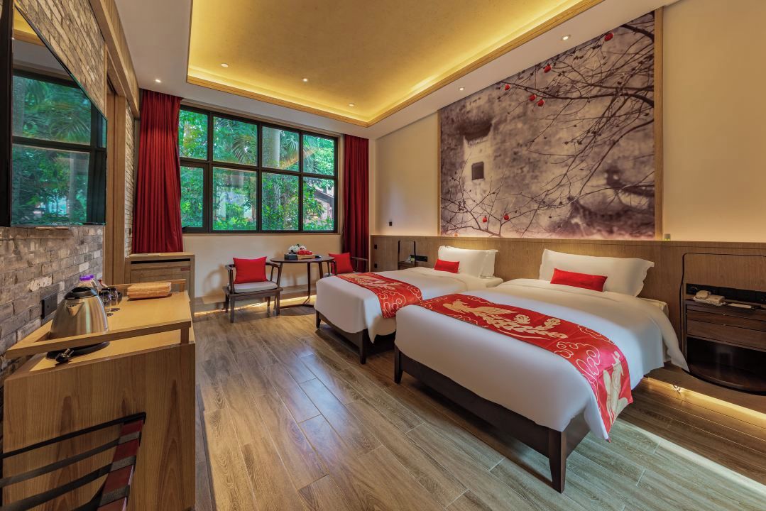 Una habitación de hotel con dos camas, un escritorio, una silla y un ventanal grande.