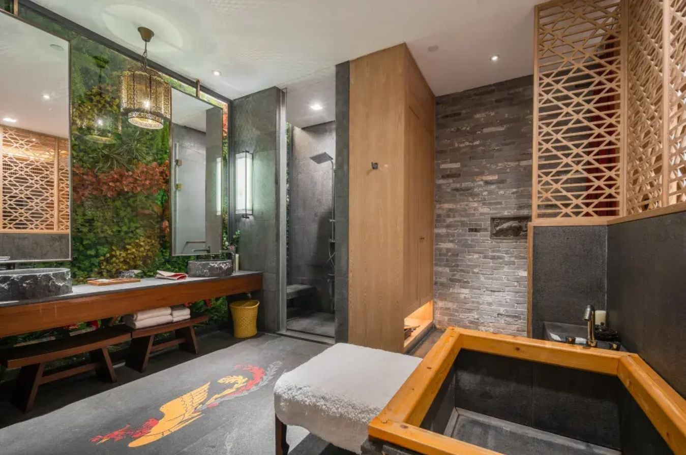 A modern bathroom with a wooden bench, a large mirror, and a stone wall.