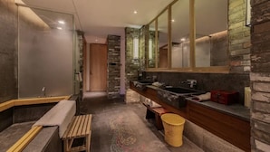 Une salle de bain moderne avec un mur en pierre, un grand miroir, un banc en bois et une baignoire.