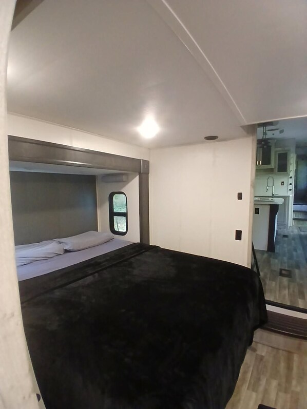 A compact room with a bunk bed, a small window, and a kitchenette area visible through an open door.