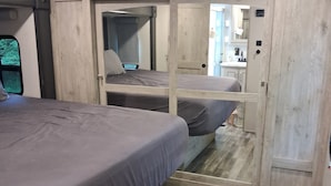 Ein gemütliches Schlafzimmer mit zwei Betten, Holzboden und einer kleinen Küche im Hintergrund.