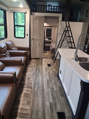 A compact RV interior with a kitchenette, a dining area with a table and chairs, and a seating area with a sofa.