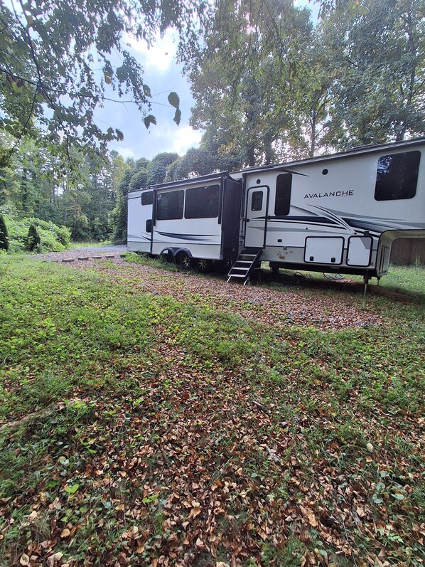 A white RV with 'Avalanche' branding parked in a wooded area.