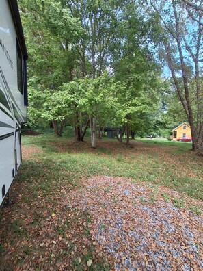 A campsite with a white RV parked on a gravel area surrounded by trees and a small yellow building.