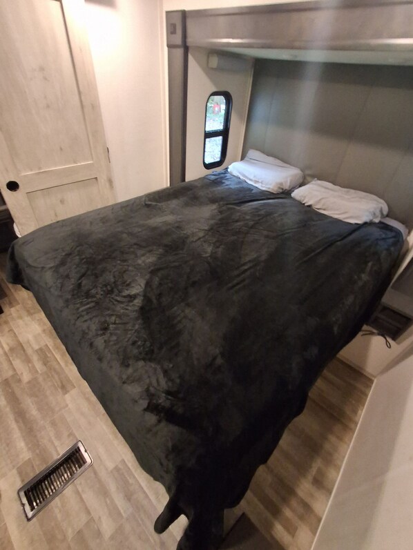 A bed with a dark cover, a bedside table with a lamp, and a window with a view.