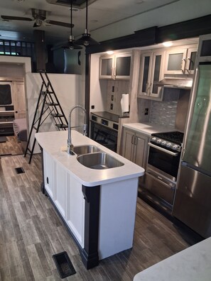 A modern kitchen with a central island, stainless steel appliances, and a ladder leaning against the wall.