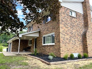 A two-story brick house with a covered porch and a small garden area. - Hot Tub | Sleeps 18 | Game Room | Near Notre Dame (South Bend)