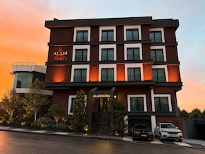 A multi-story hotel with a modern design, featuring a prominent entrance and a parking area with two cars. - Alabi Hotels İstanbul (İstanbul)