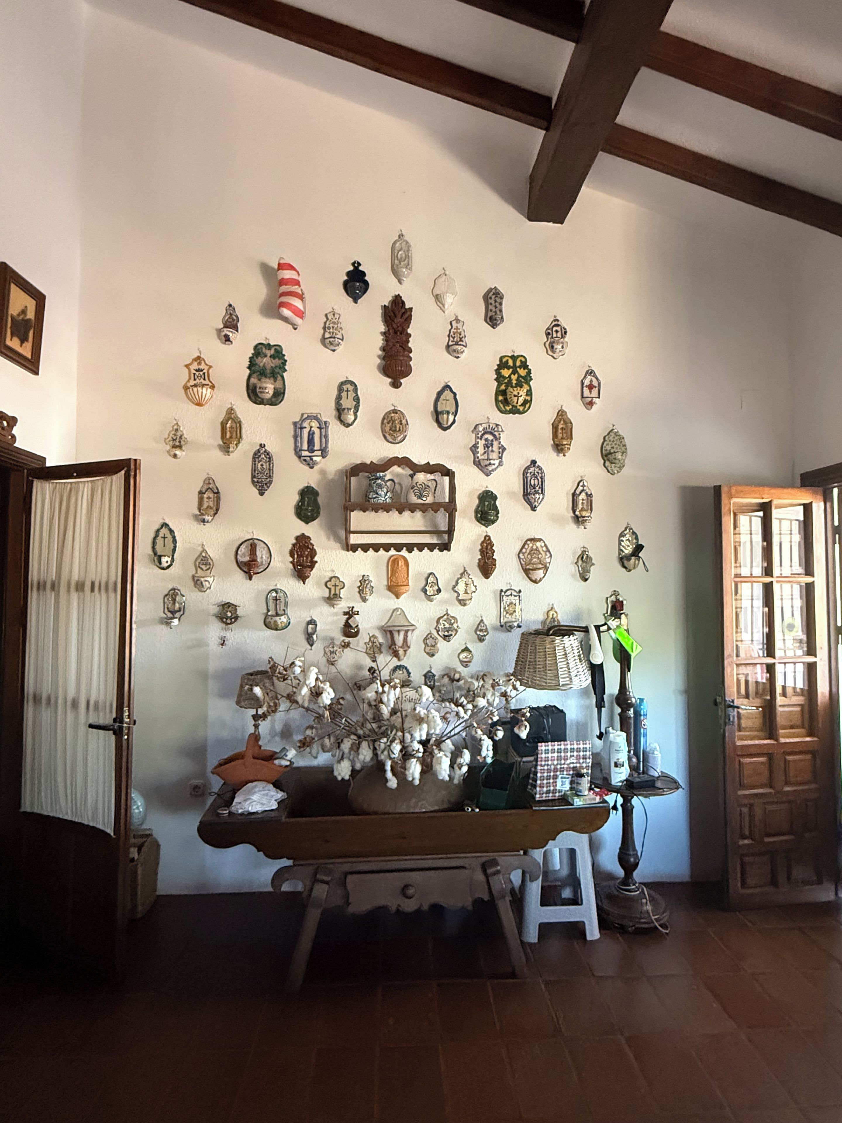 Una habitación con una pared decorada con varios objetos ornamentales y una mesa con una lámpara y un jarrón de flores.