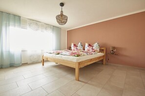 A bedroom with a wooden bed, a window with curtains, a wall-mounted lamp, and a radiator. - Riesling at the Regnery winery (Klüsserath)