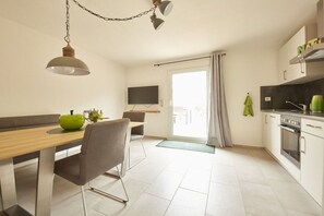 A modern kitchen with a dining area, a TV mounted on the wall, and a view through a glass door. - Riesling at the Regnery winery (Klüsserath)