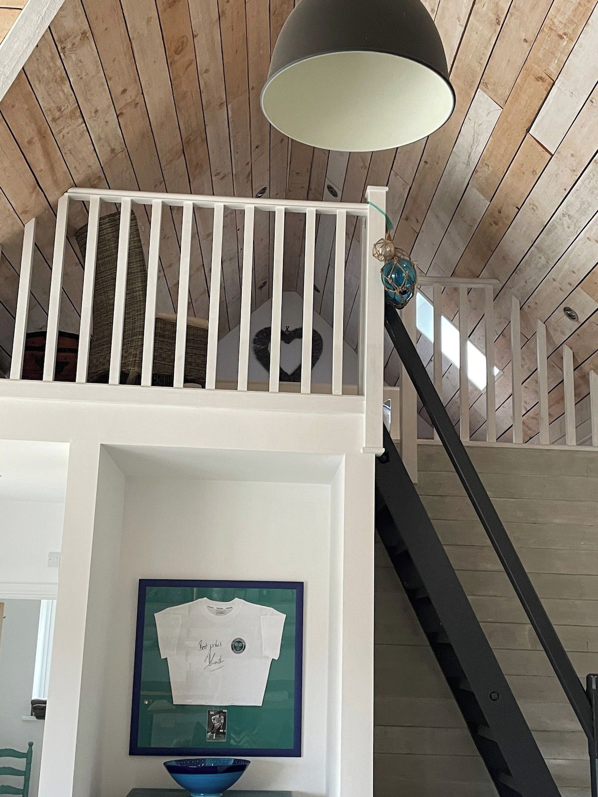 A room with a white railing, a framed item on the wall, and a staircase.