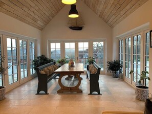 Una habitación amplia con techo alto, ventanas grandes, una mesa de comedor central y varios conjuntos de asientos.