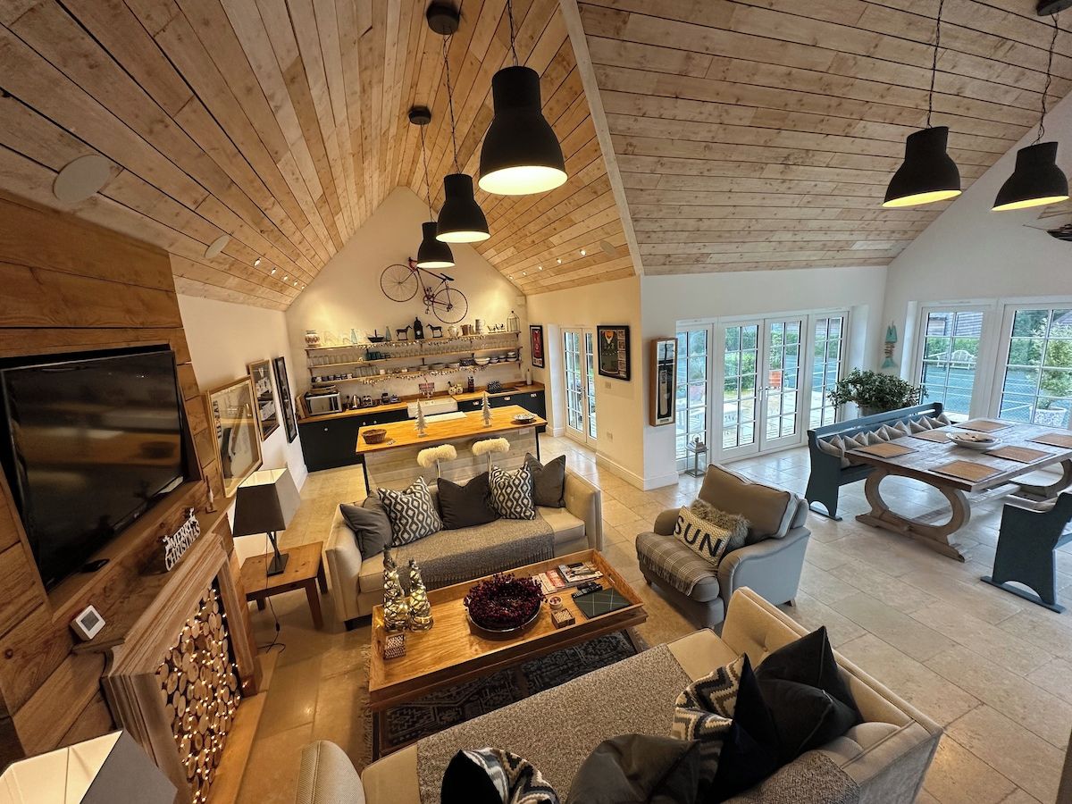 A spacious living area with a high ceiling, wooden beams, a large TV, and a dining area with a table and chairs.