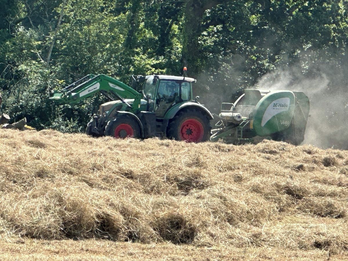 Un tracteur avec une presse à balles dans un champ.