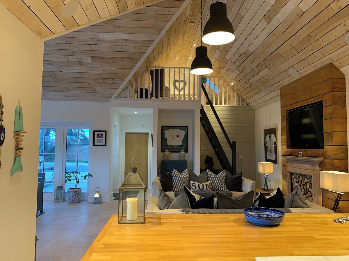 Een gezellige woonkamer met een houten plafond, een trap, een open haard en een televisie.