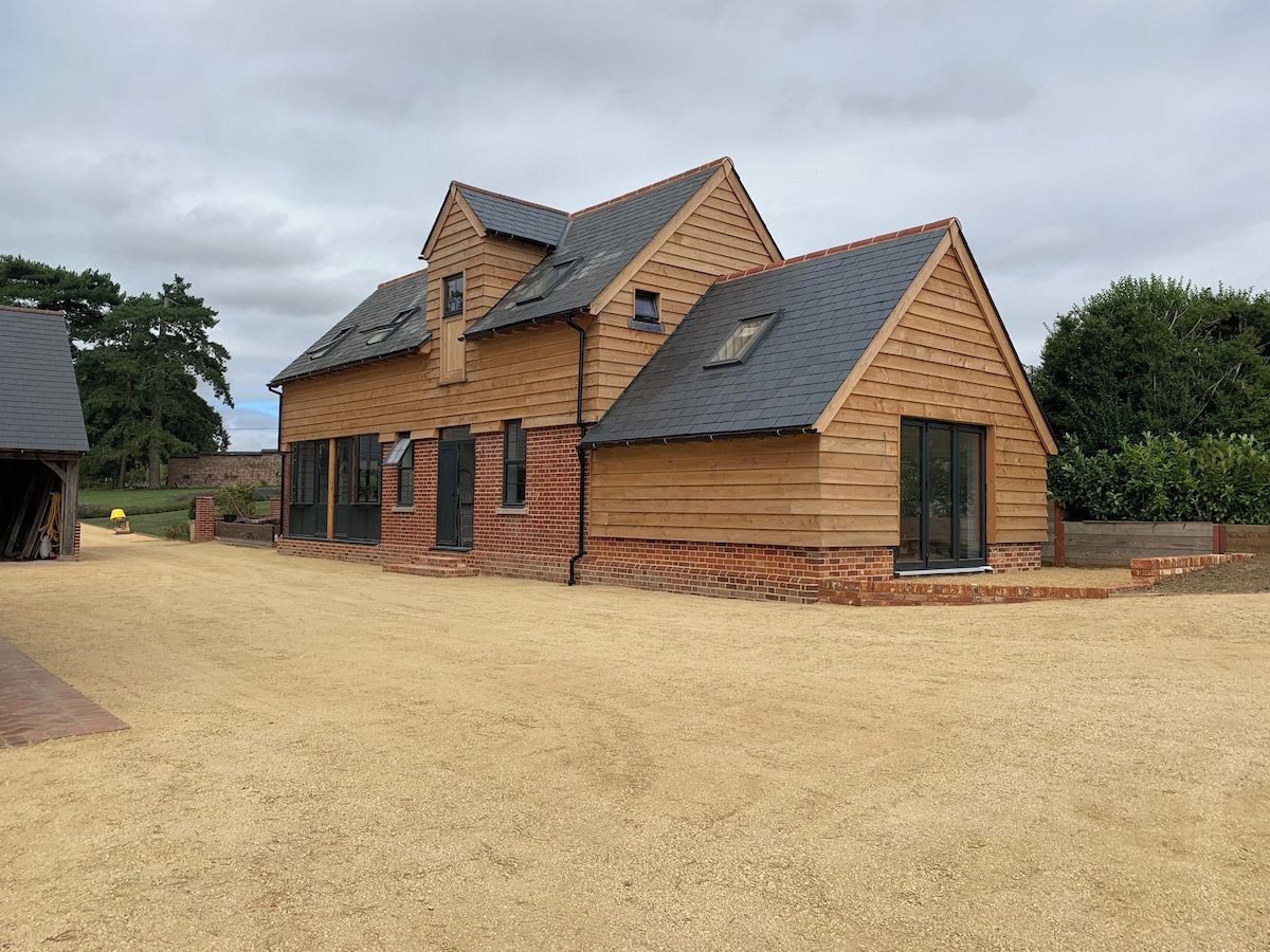 A two-story wooden house with a sloped roof, a garage, and a gravel driveway.