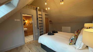 Un dormitorio con un entrepiso con zona de dormir, una cama con ropa de cama blanca, una lámpara de noche y un tragaluz.