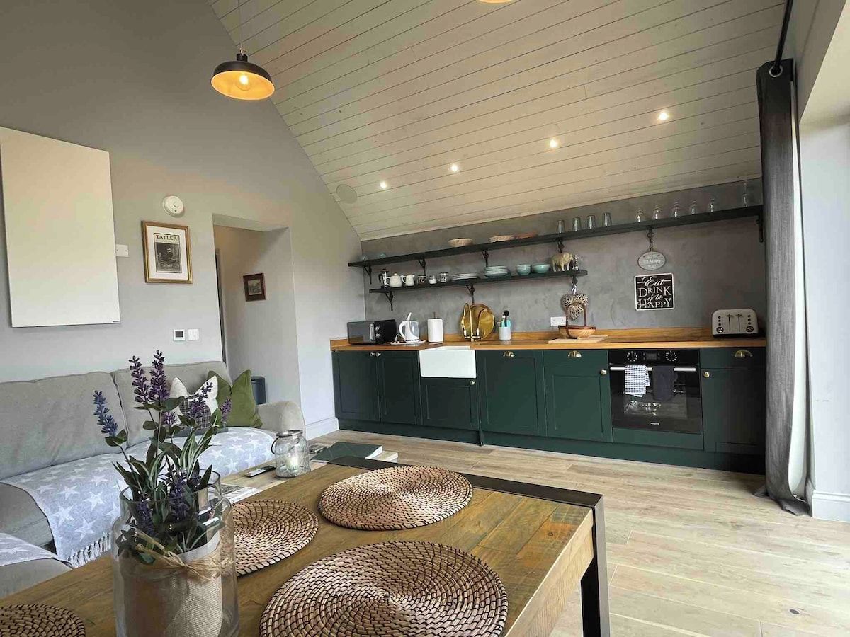 Una cocina moderna con armarios verde oscuro, encimera de madera y lámpara colgante.