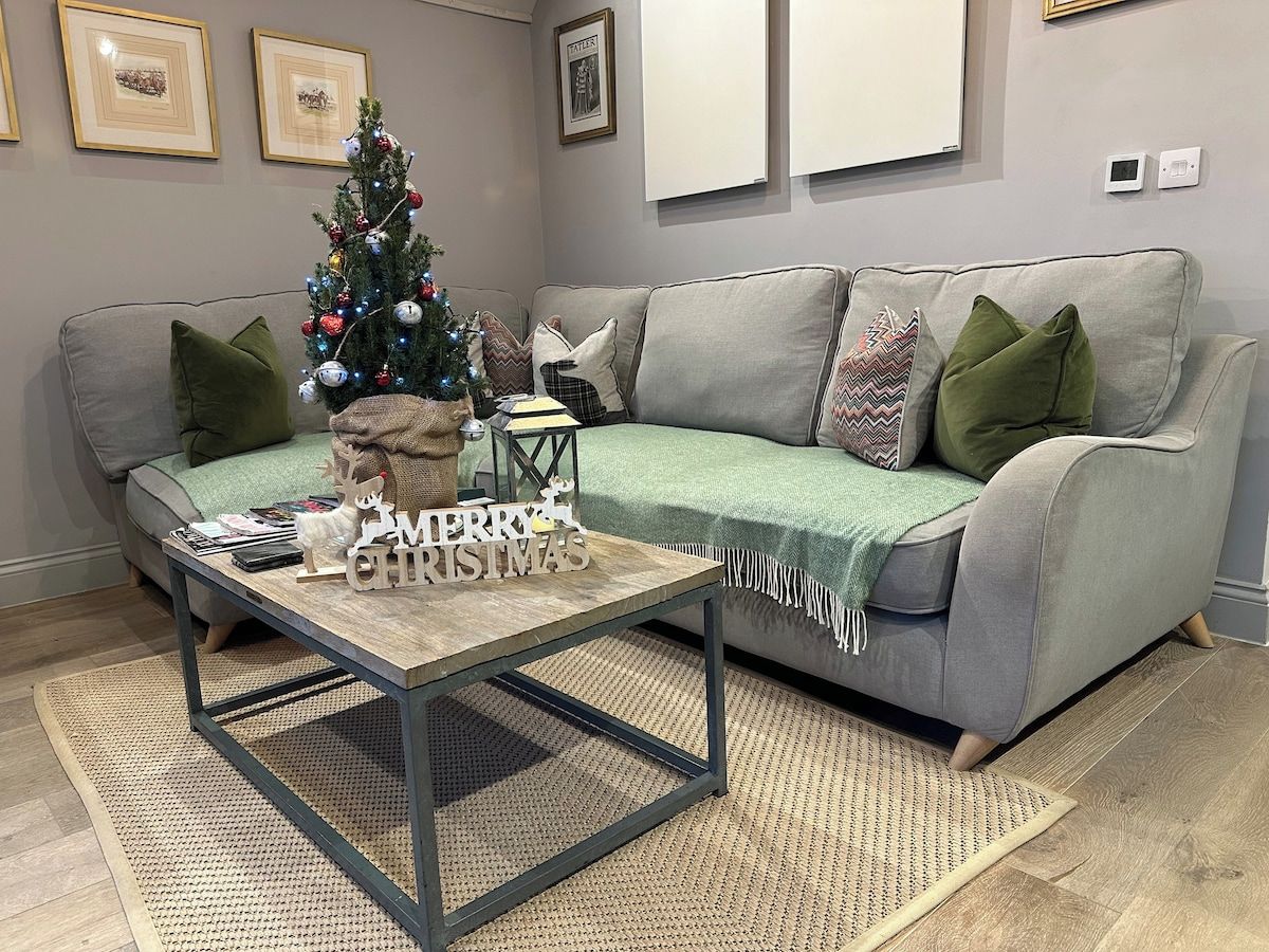 A living room with a grey sofa, a coffee table, a Christmas tree, and a fireplace.