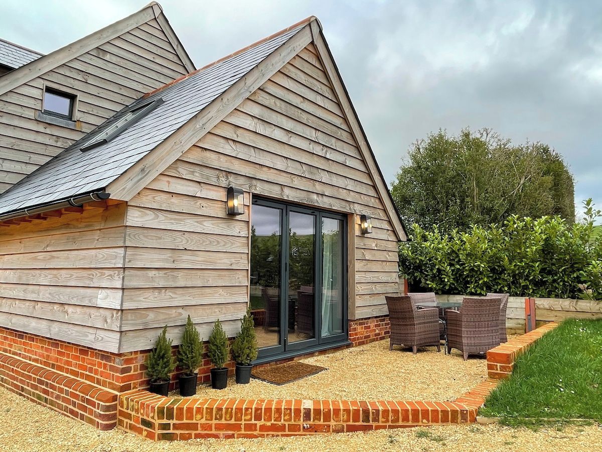 A wooden house with a sloped roof, a glass door entrance, and a patio area with outdoor furniture.
