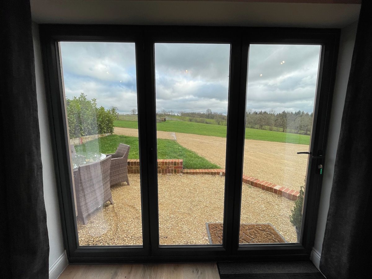 A room with a large window overlooking a grassy field and a brick structure.