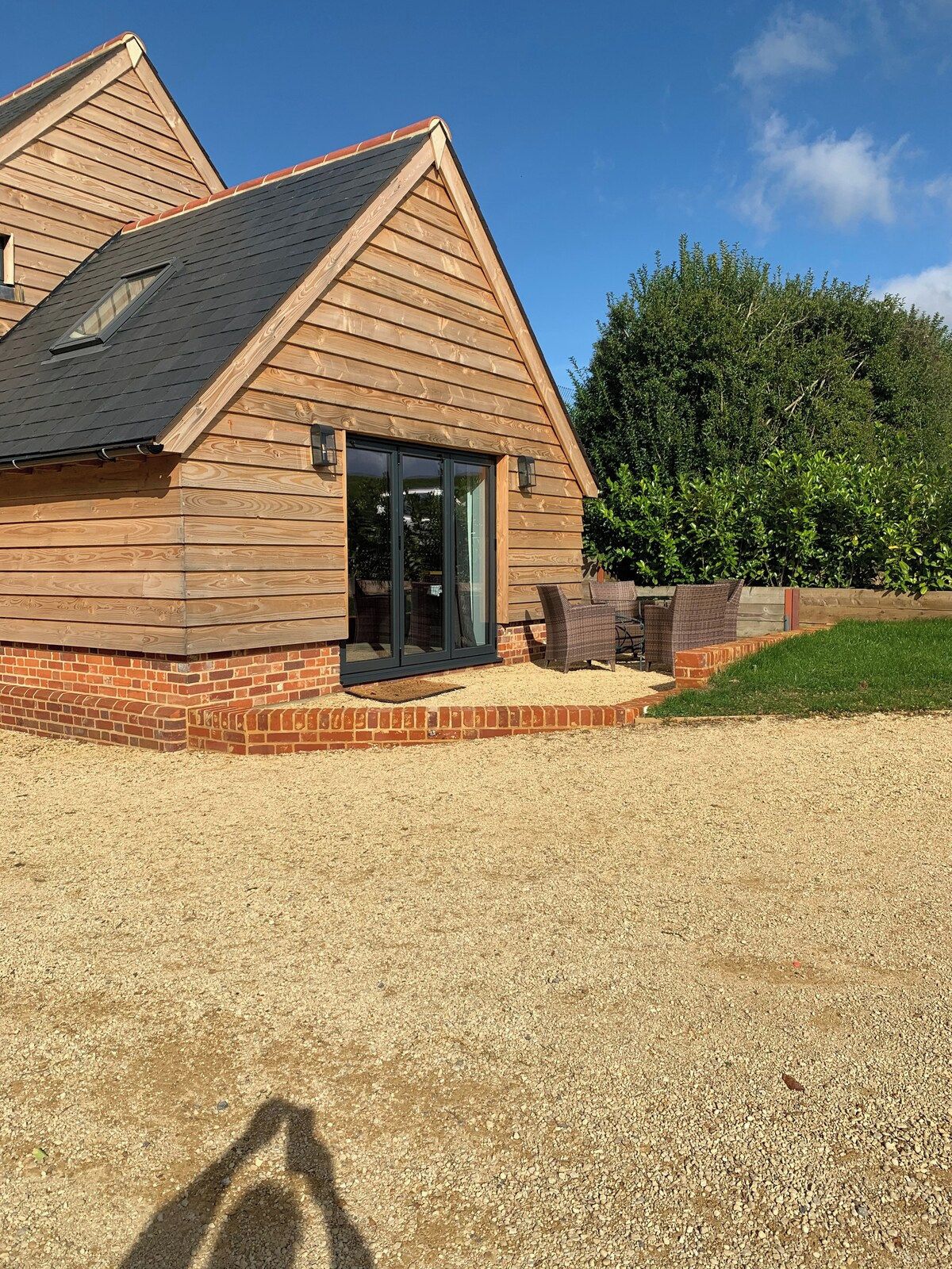 A wooden building with a sloped roof, a brick foundation, and a gravel driveway.