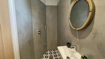 Un baño con ducha, un lavamanos con artículos de aseo y un espejo redondo en la pared.