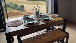 Et spisebord dækket med tallerkener, glas og en vase med blomster, placeret nær et vindue med udsigt over et mark.