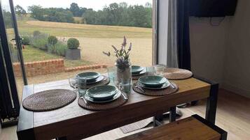 A dining table set with plates, glasses, and a vase with flowers, positioned near a window with a view of a field.