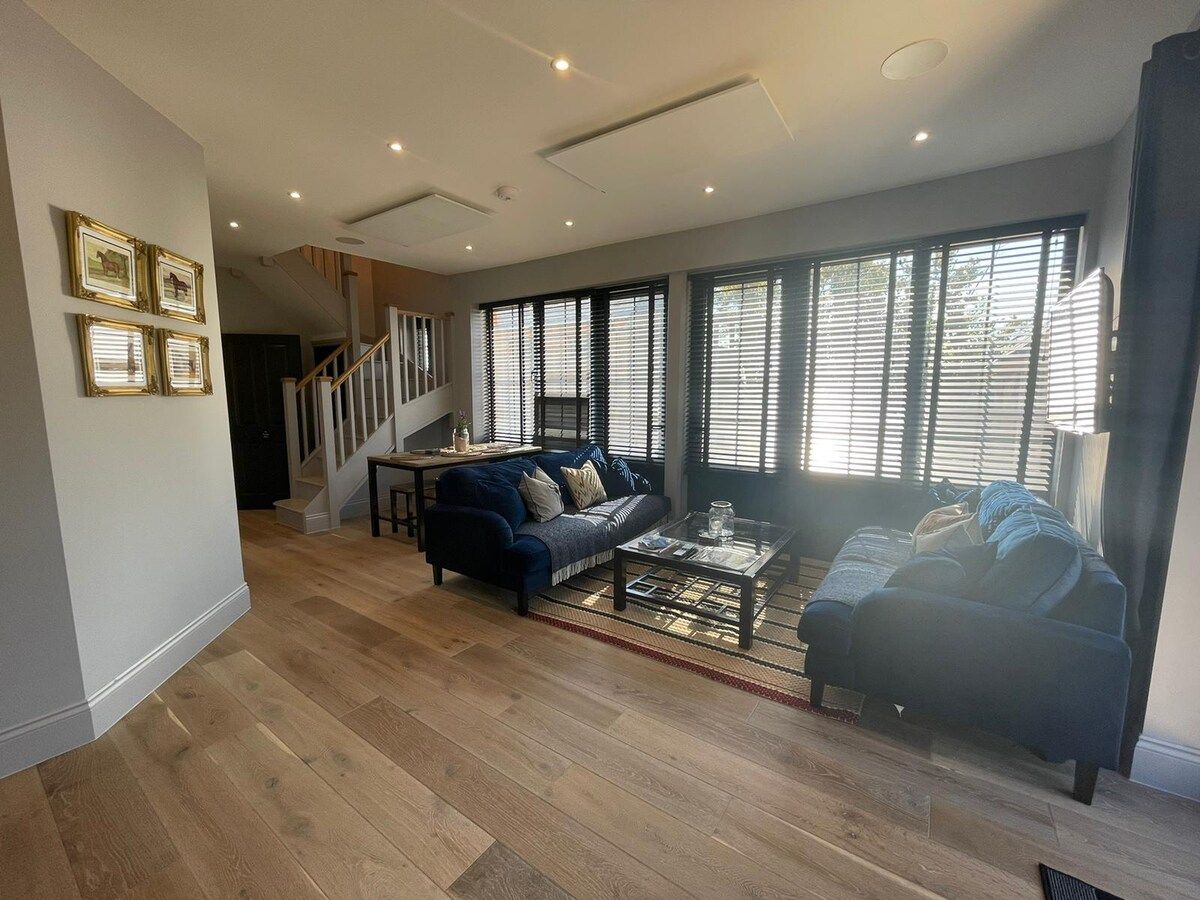 A spacious living room with a staircase, a sofa, a coffee table, and large windows.