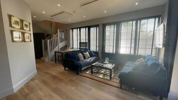 A spacious living room with a staircase, a sofa, a coffee table, and large windows.