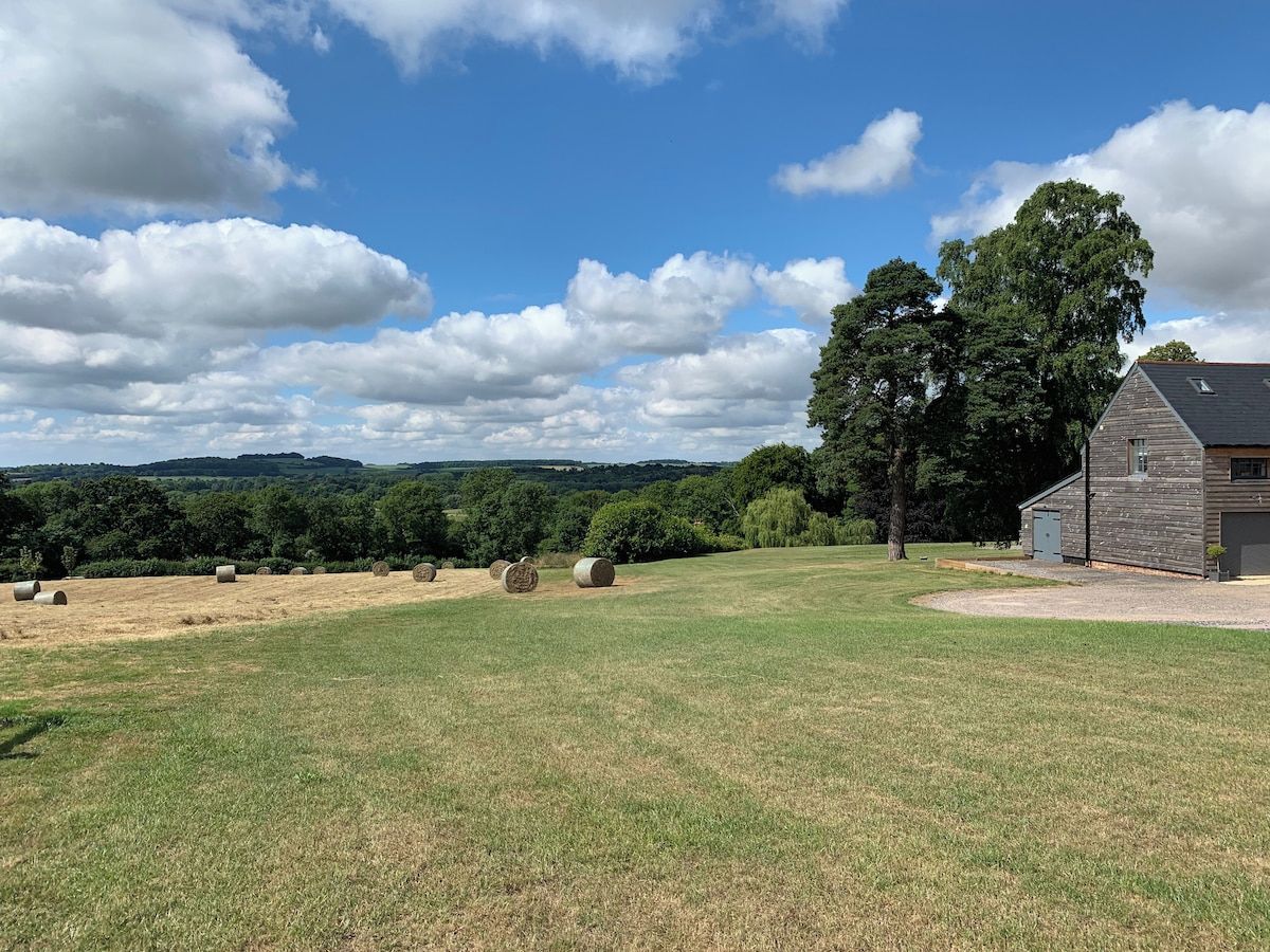 Un paysage rural avec une grange, des bottes de foin et un ciel dégagé.