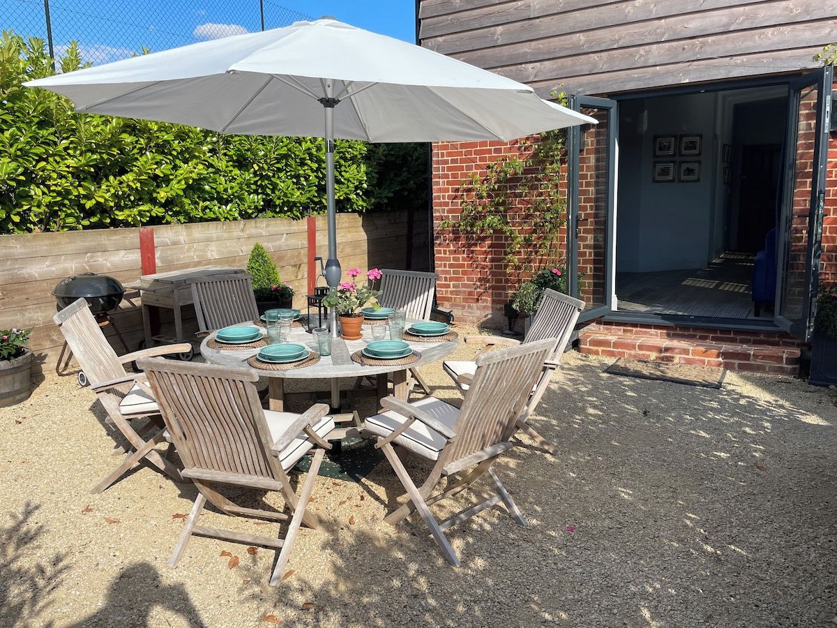 Een terras buiten met een ronde tafel, stoelen en een grote parasol.