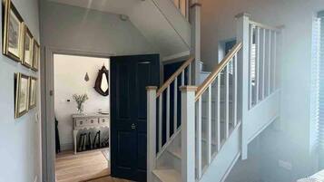 A modern interior with a wooden staircase, a dining area, and a hallway leading to a dark door.