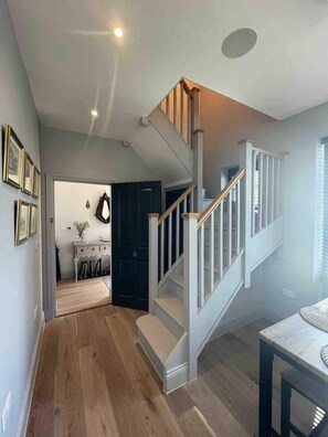 Un interno moderno con una scala in legno, una zona pranzo e un corridoio che conduce a una porta scura.