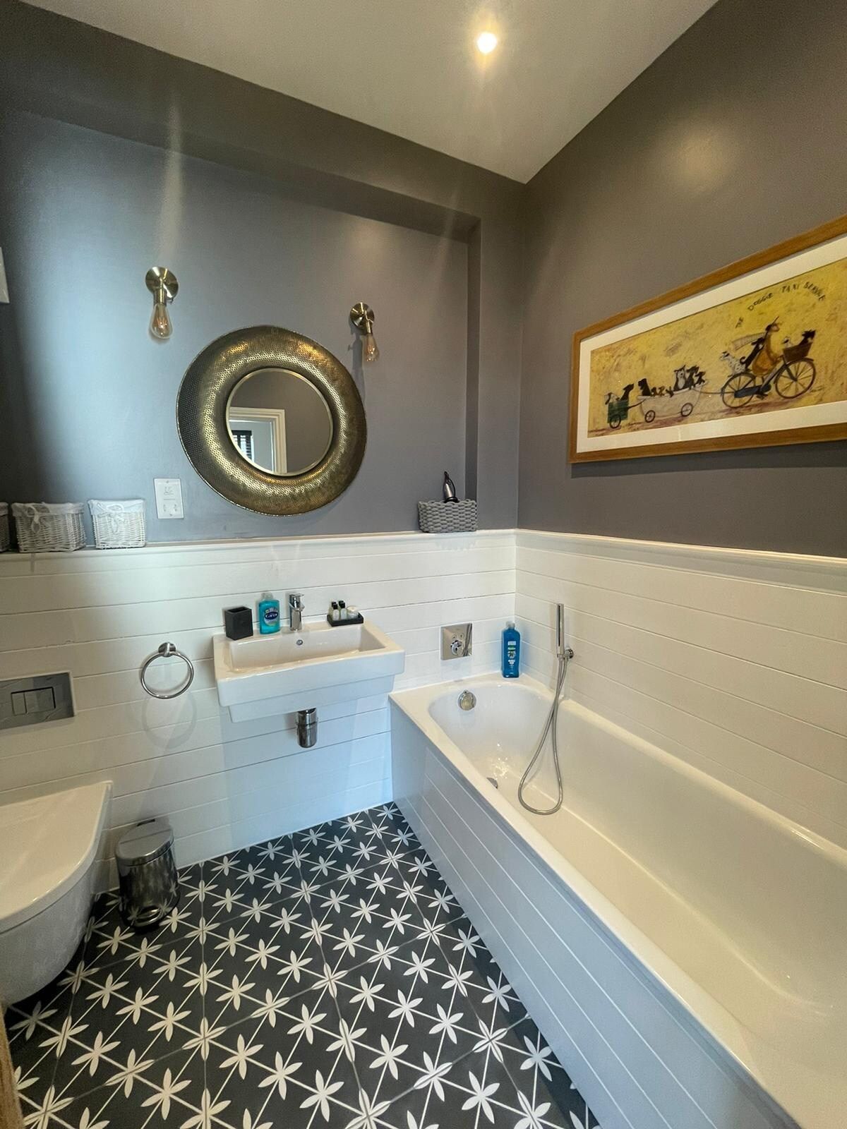 A bathroom with a bathtub, a sink, a mirror, and a wall-mounted light fixture.