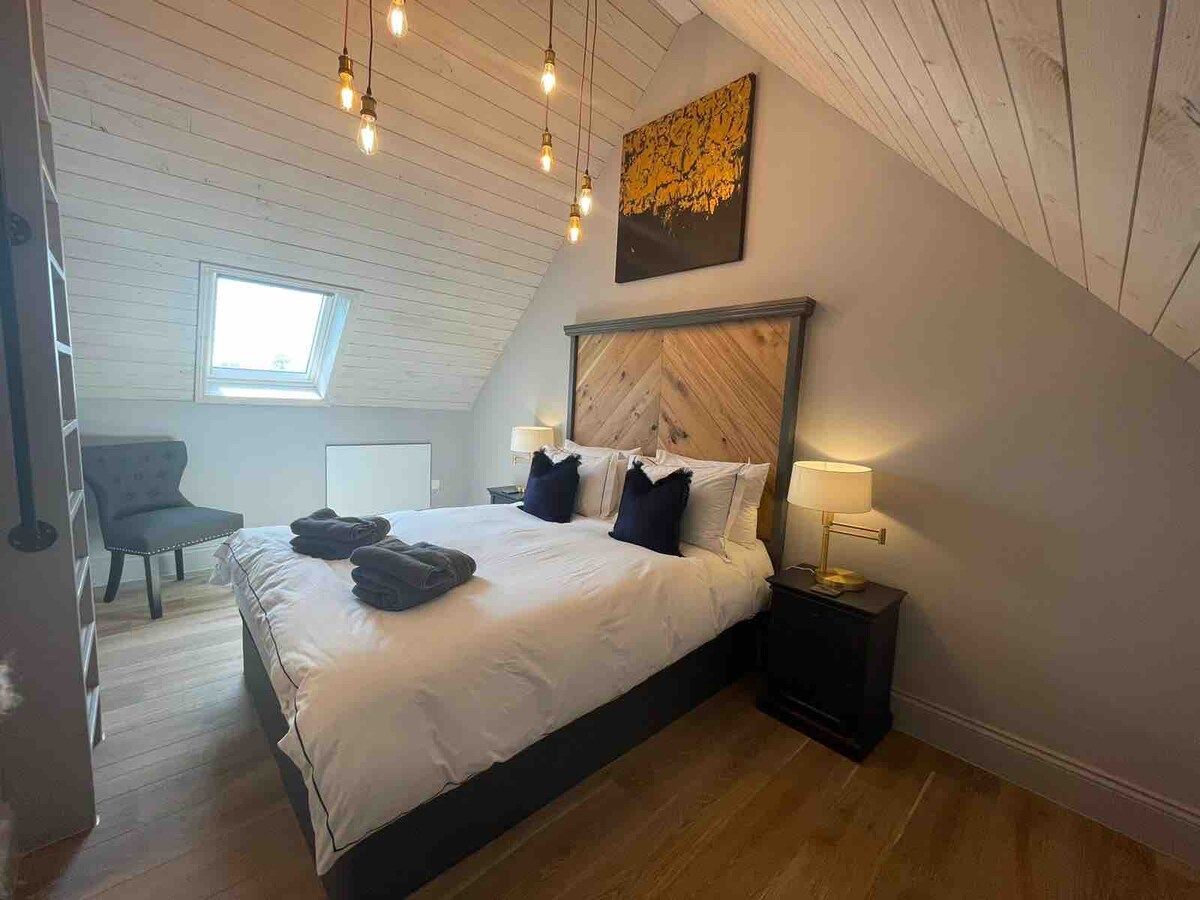 Een slaapkamer met een groot bed, een nachtkastje, een lamp, een stoel en een dakraam.