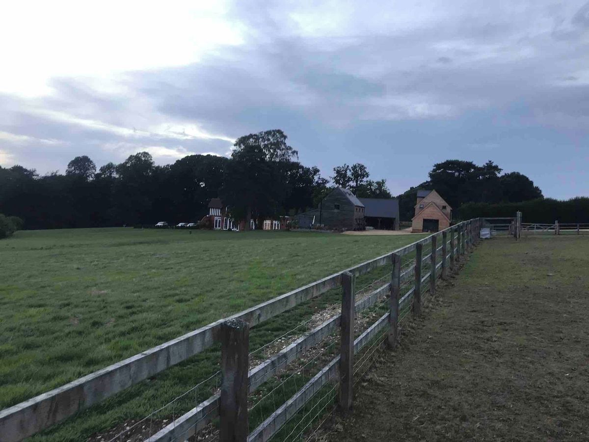 A fenced field with a building and a small structure in the distance.