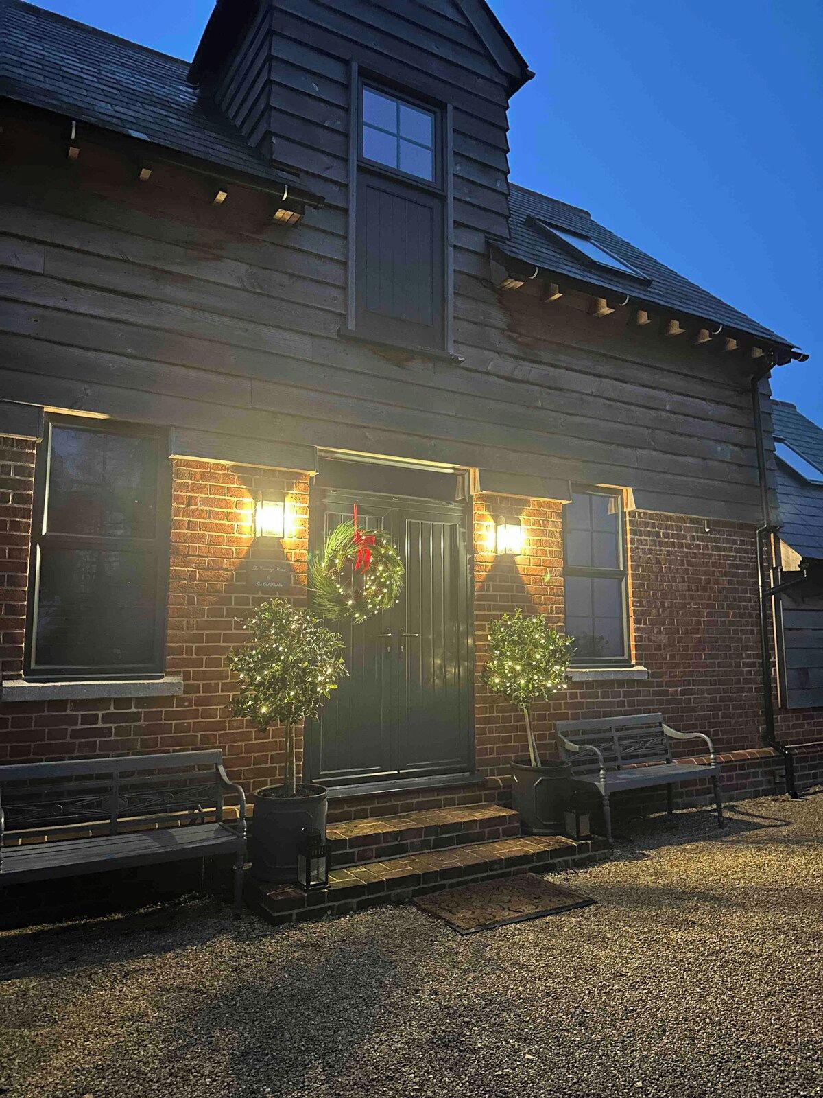 Una casa a due piani in legno con rivestimento in mattoni, una porta d'ingresso decorata con una ghirlanda e due panchine all'esterno.